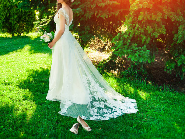 lockige brünette Braut mit einem Hochzeitsstrauß aus Blumen und posiert - Foto, Bild