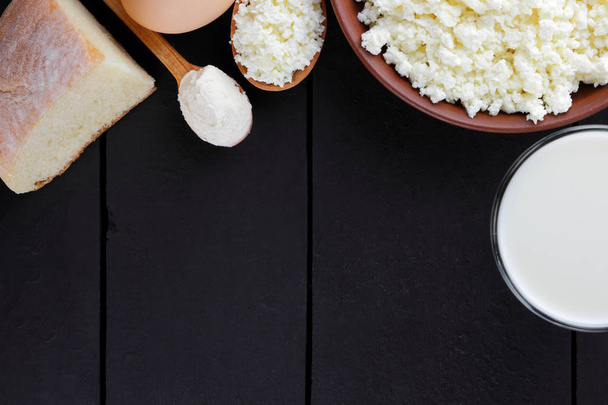 Cottage cheese and eggs on a dark background, assorted dairy products on dark boards, milk in a glass, soft cheese in a clay plate, wooden cutlery, rustic style, copy space, bread - Foto, immagini