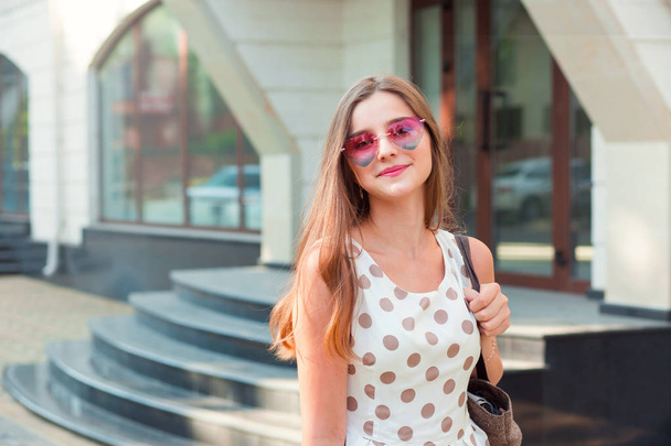 lány hosszú barna hajjal, rózsaszín szív alakú napszemüveg mosolyogva szabadban - Fotó, kép