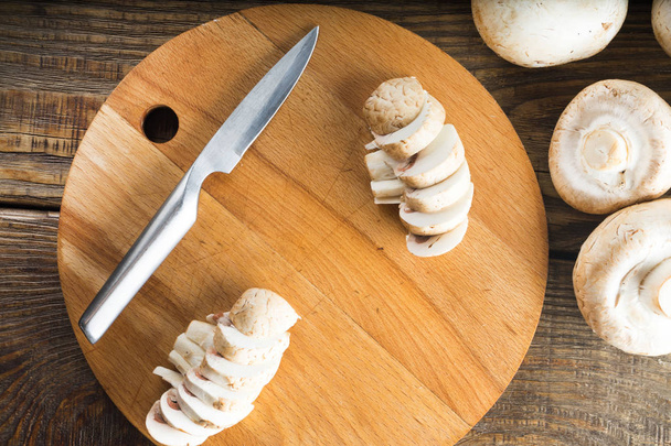 Champignon mushrooms and a knife on a wooden cutting board. - Фото, изображение