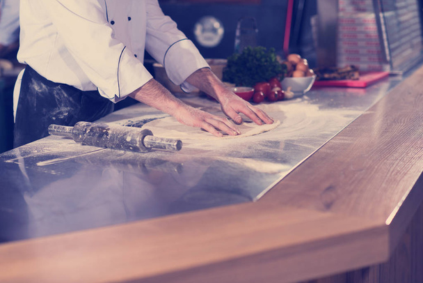 chef preparing dough for pizza rolling with hands on sprinkled with flour table - Foto, Imagem
