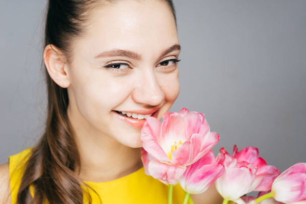 beautiful young girl in yellow dress smiling, holding fragrant pink flowers - Foto, Imagen