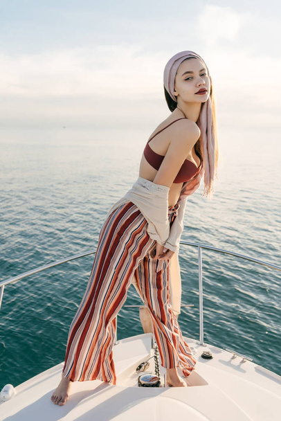 gorgeous rich woman in stylish summer clothes posing on her white yacht against the blue calm sea - Fotoğraf, Görsel