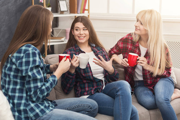 Drie jonge vriendinnen met koffie thuis chatten - Foto, afbeelding
