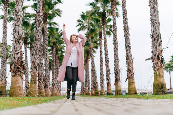uma jovem garota ativa em roupas elegantes caminha pelo parque, cercada por palmas verdes e plantas
 - Foto, Imagem