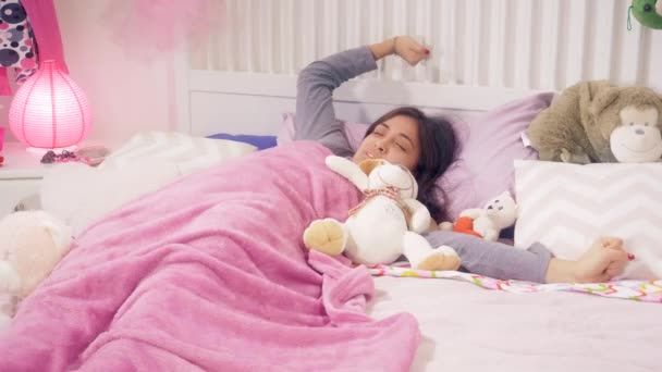 Mujer joven durmiendo en la cama con peluche de juguete despertando por la mañana
 - Metraje, vídeo