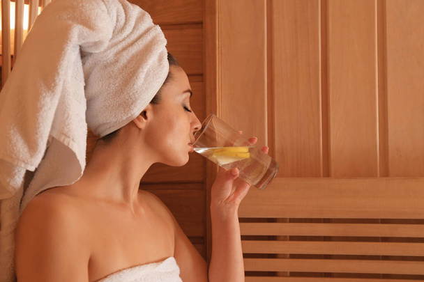 Young beautiful woman drinking cold water with lemon in sauna - Foto, imagen
