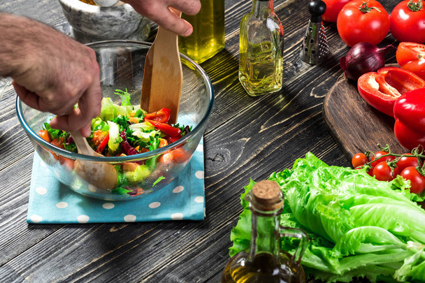 Mies valmistaa salaattia tuoreilla vihanneksilla puupöydällä. Ruoanlaitto maukasta ja terveellistä ruokaa. lähikuva
 - Valokuva, kuva