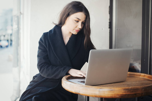 Молода жінка працює на ноутбуці в кафе
. - Фото, зображення