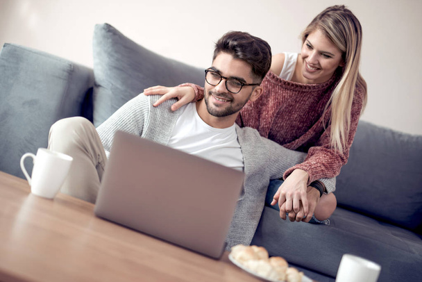 Giovane coppia amorevole con caffè utilizzando il computer portatile sul divano a casa
. - Foto, immagini