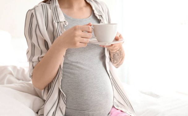 Beautiful pregnant woman drinking coffee on bed in morning - 写真・画像