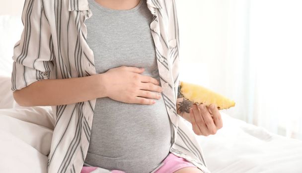 Beautiful pregnant woman with slice of pineapple on bed in morning - Photo, Image