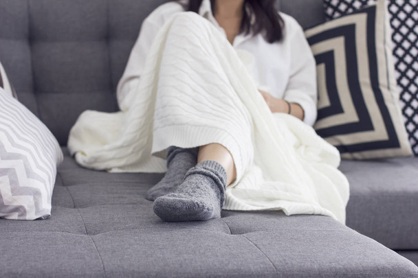 Young woman sitting on sofa covered in blanket, focus on her grey socks - Foto, Bild