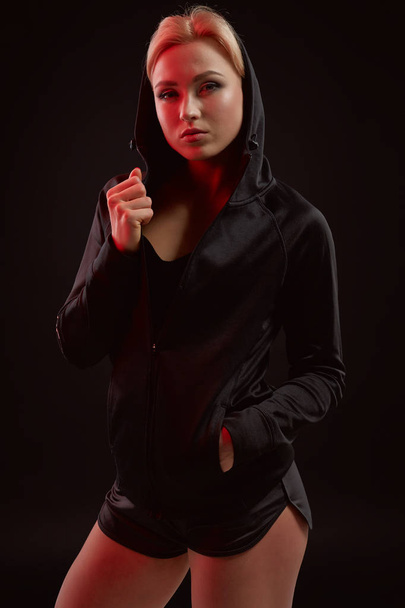 Belle fille sportive séduisante avec la silhouette sexy mince dans le sweat à capuche noir, sous-vêtements de sport et petit short noir pose en studio
 - Photo, image
