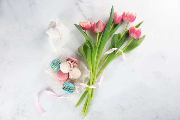 Plat lag compositie met heerlijke macarons, tulpen en gift box op lichte achtergrond - Foto, afbeelding