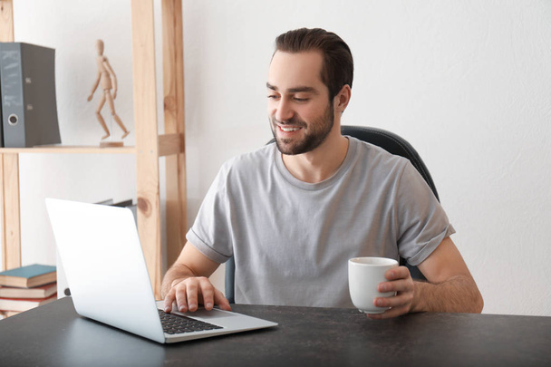 Freelancer masculino que bebe té mientras trabaja con un portátil en su oficina en el hogar
 - Foto, imagen
