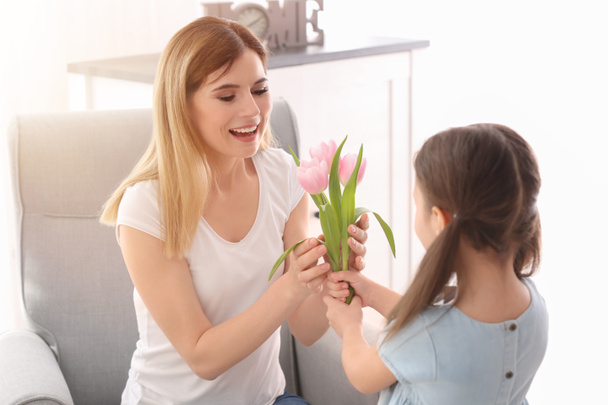 Mother receiving flowers from her cute little daughter at home - Foto, Bild