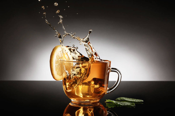 Чашка лимонного чая с брызгами на темном фоне
 - Фото, изображение
