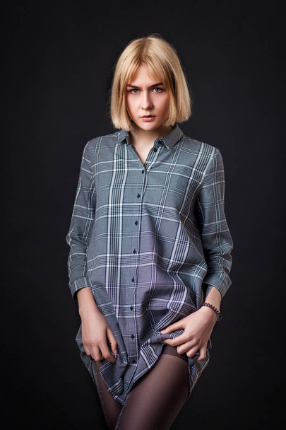Beautiful young blonde woman with a square in a gray dress shirt showing beautiful legs and posing on a black isolated background - Фото, зображення
