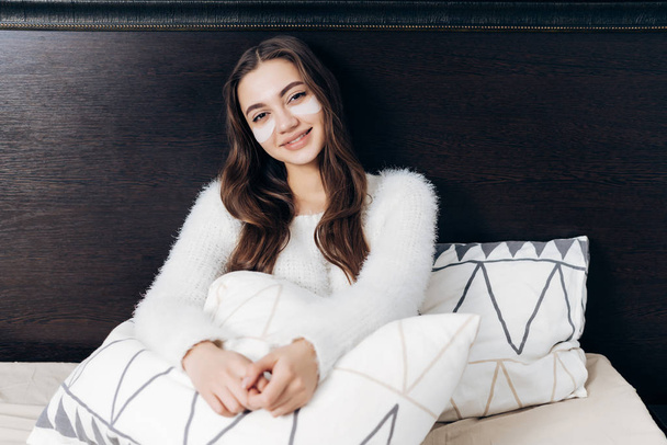 beautiful long-haired girl lies in bed early in the morning, under the eyes of white patches, smiling - Foto, Bild