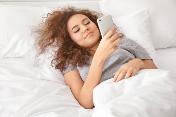 Mattina di giovane donna afro-americana sdraiata a letto con cellulare
 - Foto, immagini