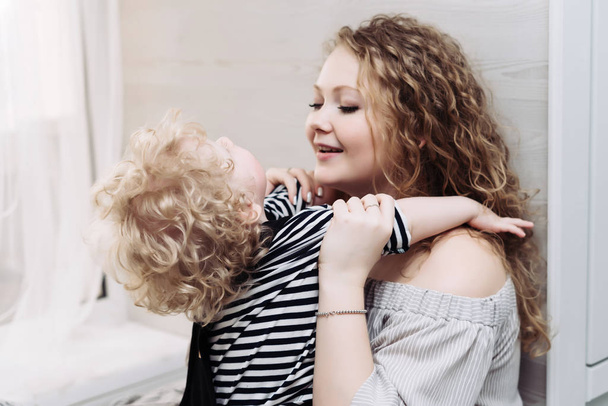 curly young mother playing with her little baby boy, laughing, having fun - Fotó, kép