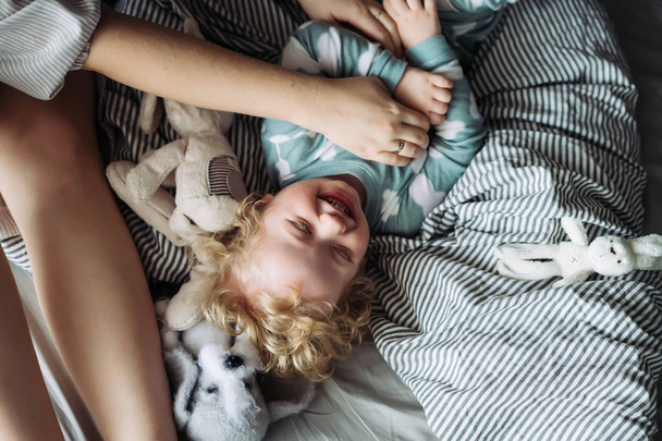 mom plays with her little baby, laughs, tickles, lies on the bed - Valokuva, kuva