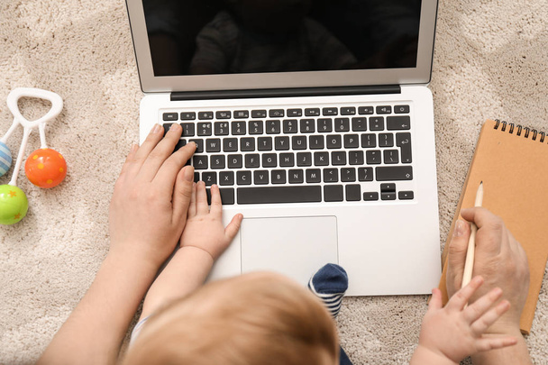 Молодая мать с ребенком, пользующаяся ноутбуком дома
 - Фото, изображение