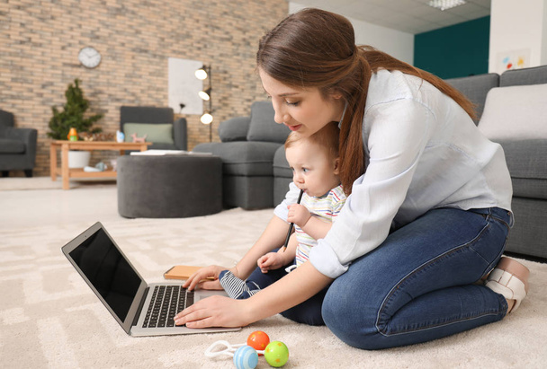 junge Mutter mit Baby arbeitet zu Hause auf Teppich - Foto, Bild
