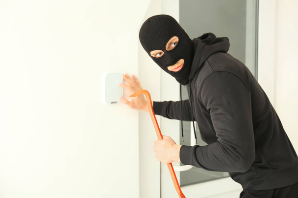 Mannelijke dief met Koevoet breken beveiligingssysteem binnenshuis - Foto, afbeelding