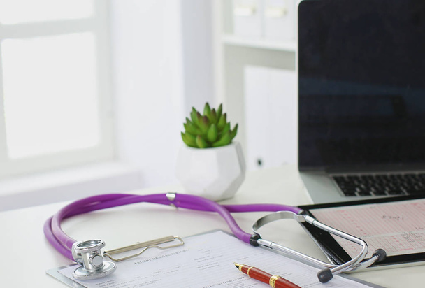 Nahaufnahme vom Schreibtisch einer Arztpraxis mit einem Stethoskop im Vordergrund und einer Flasche mit Pillen im Hintergrund - Foto, Bild