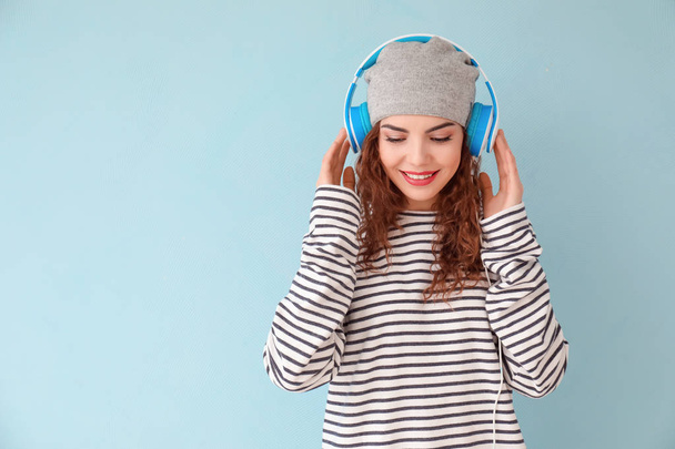 Beautiful young woman with headphones listening to music on color background - Foto, Bild
