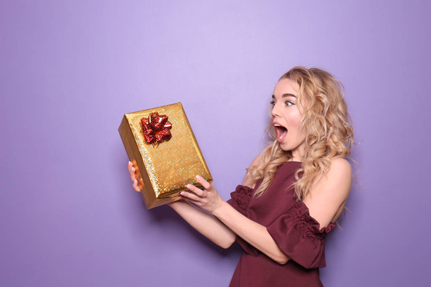 Здивована молода жінка з подарунковою коробкою на кольоровому фоні
 - Фото, зображення