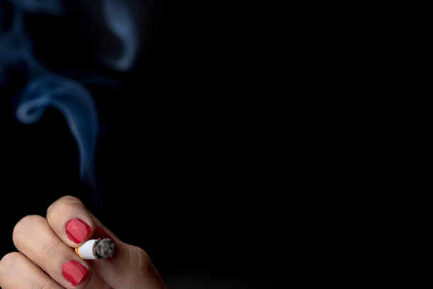 Τσιγάρο με τον καπνό στο χέρι γυναίκα με κόκκινο νύχι που απομονώνονται σε μαύρο φόντο με αντίγραφο χώρο για το κείμενο. Γυναίκα το κάπνισμα. Κακή συνήθεια μπορεί να προκαλέσει καρκίνο του πνεύμονα. Τόνισε γυναίκα με νικοτίνη εθισμένος έννοια - Φωτογραφία, εικόνα