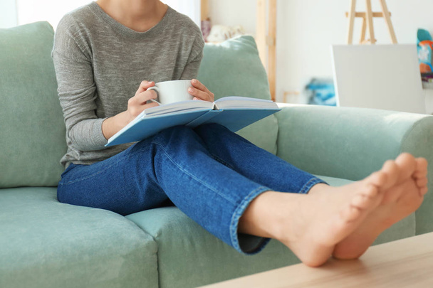 Jovem mulher bebendo café enquanto lê livro em casa
 - Foto, Imagem