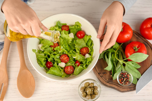 Woman adding olive oil into bowl with fresh vegetable salad on table - Foto, imagen