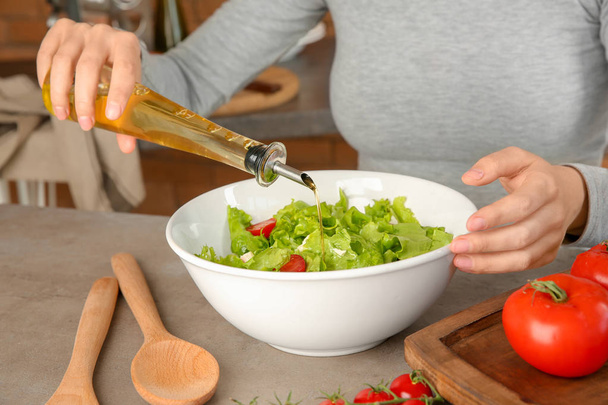 Woman adding olive oil into bowl with fresh vegetable salad on table - Фото, зображення