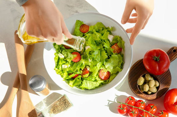Mujer agregando aceite de oliva en un tazón con ensalada de verduras frescas en la mesa
 - Foto, imagen