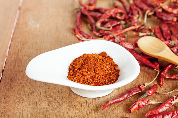 Cayenne pepper in white dish and dried chilli on wood table. - Фото, изображение