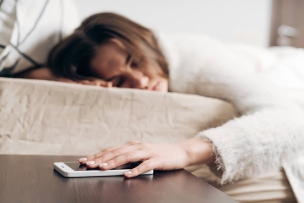 sleepy young girl sleeping in bed, can not hear the alarm on her smartphone - Photo, image