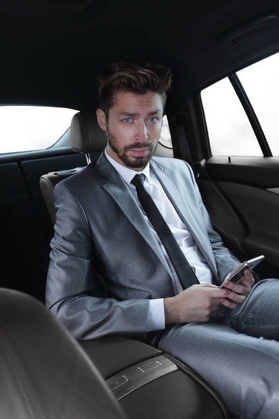 man in suit sitting in car and reading messages on smartphone - Fotoğraf, Görsel