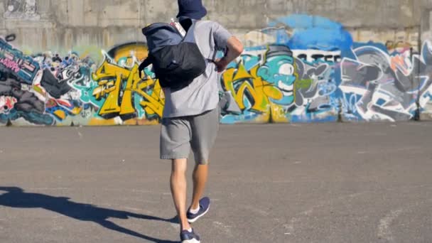 Artista de graffiti está levantando sua mochila com latas de tinta e indo em direção à parede de graffiti
 - Filmagem, Vídeo