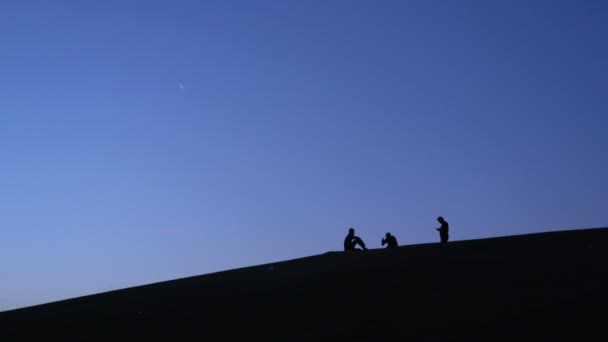Sylwetki trzech facetów, co zdjęcie na smartfonie i Selfie na stoku wzgórza wcześnie rano z młody księżyc na firmamencie nieba. - Materiał filmowy, wideo