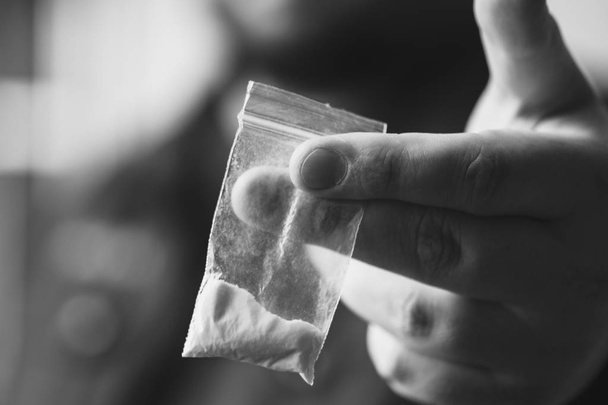 La mano del hombre sostiene un paquete o bolsa de plástico con cocaína u otras drogas, abuso de drogas y concepto de adicción al peligro
 - Foto, imagen