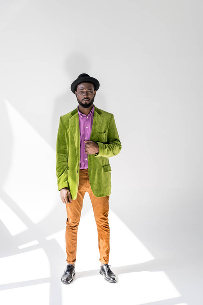 young african american man in fashionable clothing and hat posing on grey backdrop - Foto, immagini