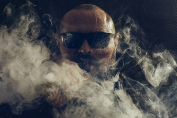 Чоловік вейп-електронна сигарета з рідиною, крупним планом, дихає великою хмарою пари або пари на темному тлі. концепція вейпінгу
 - Фото, зображення