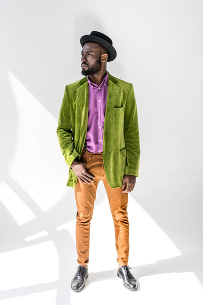 nachdenklicher afrikanisch-amerikanischer Mann in modischer Kleidung und Hut posiert auf grauem Hintergrund - Foto, Bild