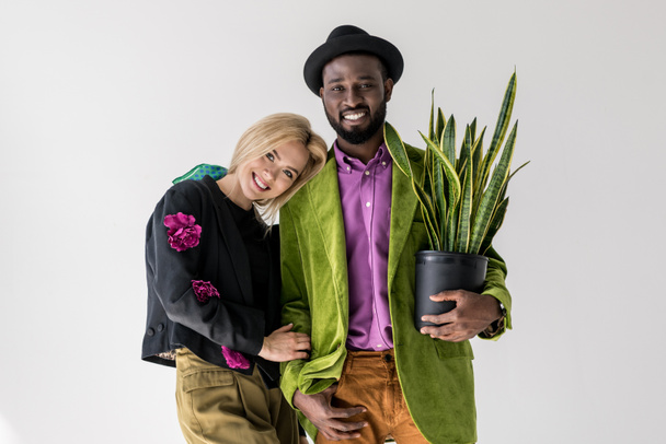 Interracial şık çift gri izole saksı poz içinde yeşil bitki ile gülümseyen portresi - Fotoğraf, Görsel