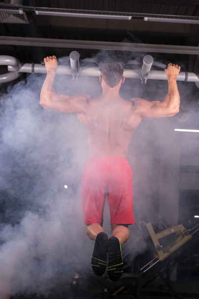 Athlete muscular fitness male model pulling up on horizontal bar in a gym. - Photo, Image