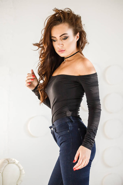 Studio portrait of beautiful brunette girl in blue jeans and black underwear standing on white wall background - Foto, afbeelding
